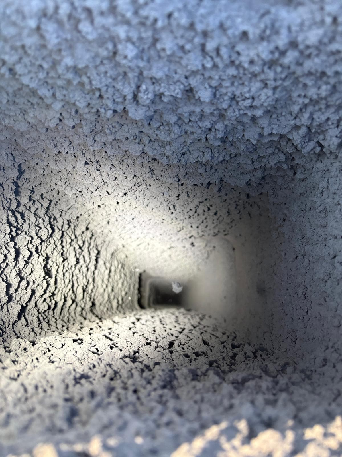 Looking down a narrow rectangular shaft heavily coated with thick, gray, clumpy soot and debris.