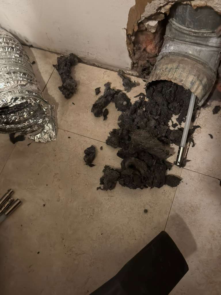 Thick dark lint removed from a metal dryer vent pipe using a cleaning tool.