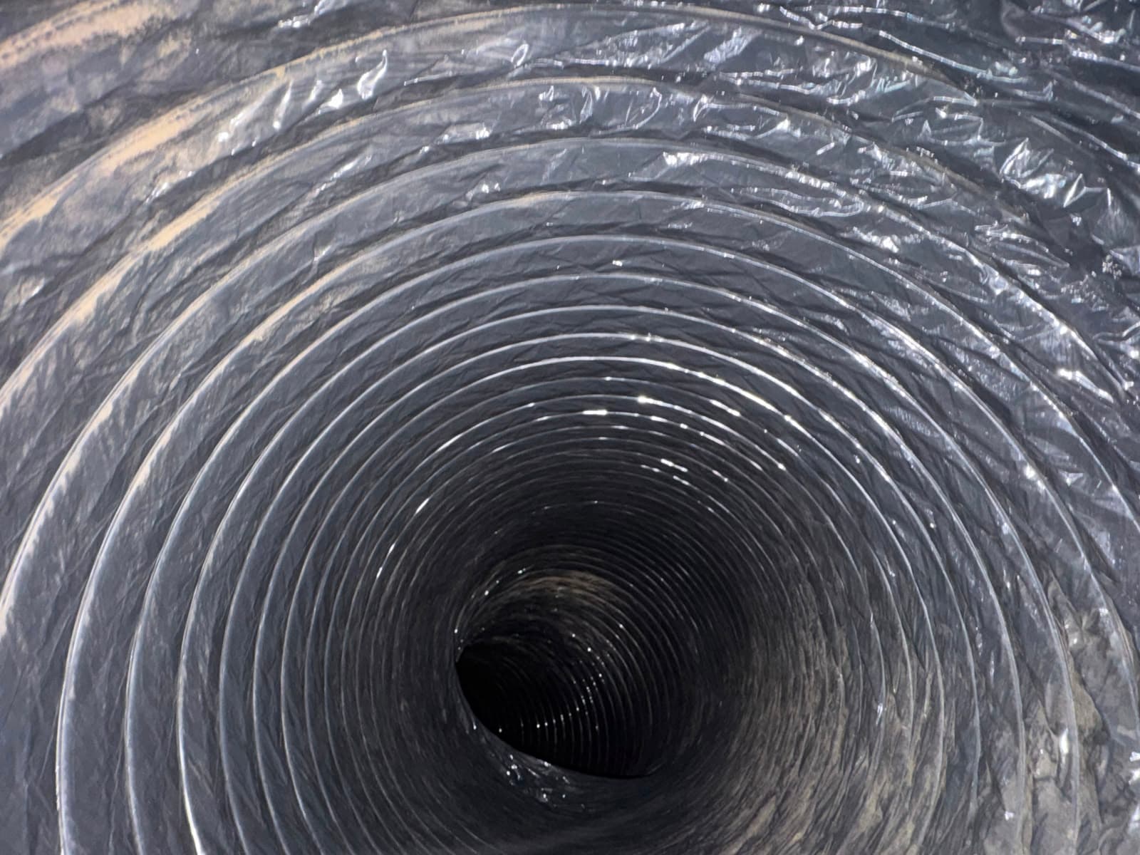 Close-up view looking through the spiraling, corrugated interior of a flexible silver ventilation duct.