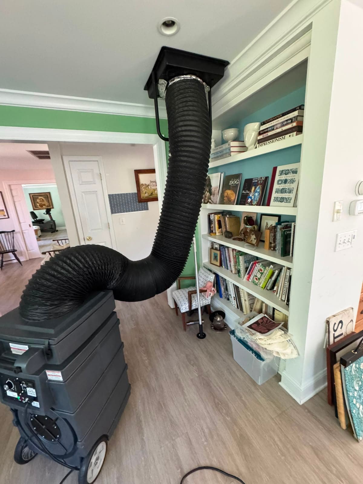 Large black flexible hose connecting a portable air filtration machine to a ceiling vent.
