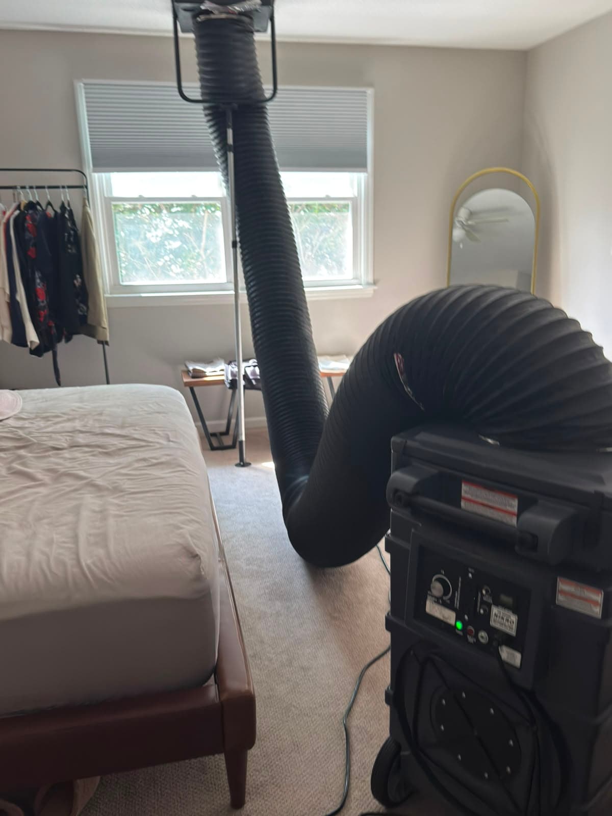 Large black hose connects a portable air filtration machine to a bedroom ceiling vent.