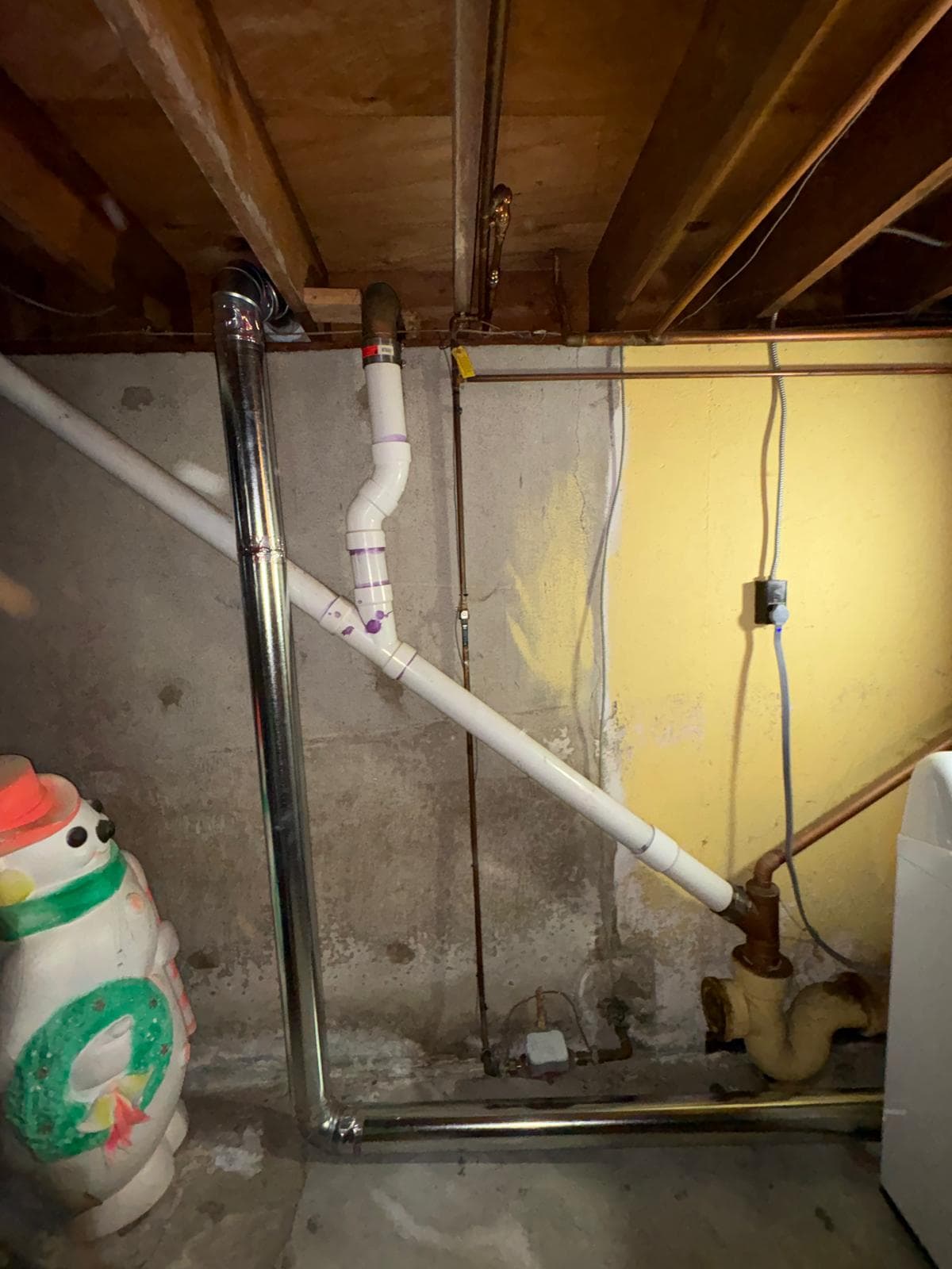 Basement plumbing with white PVC pipes, a silver vent, and a large snowman decoration.