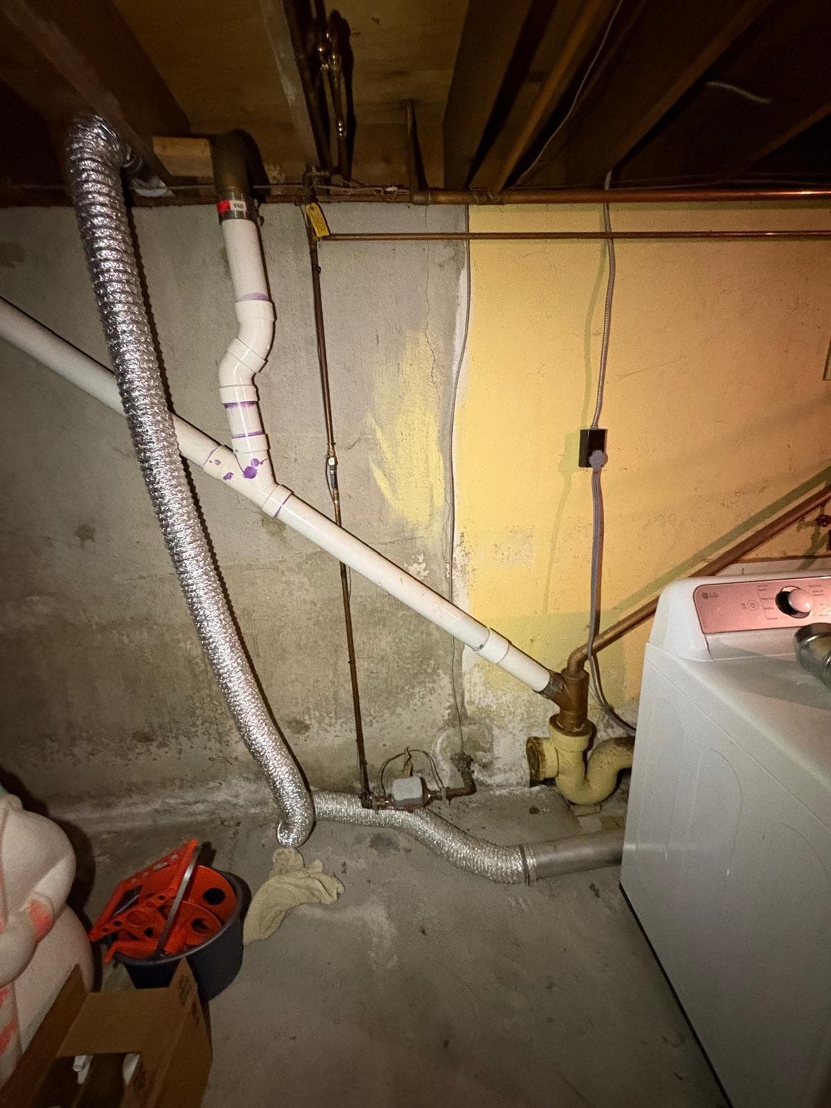 Basement plumbing featuring white PVC drain pipes, a silver dryer vent, and a washing machine.