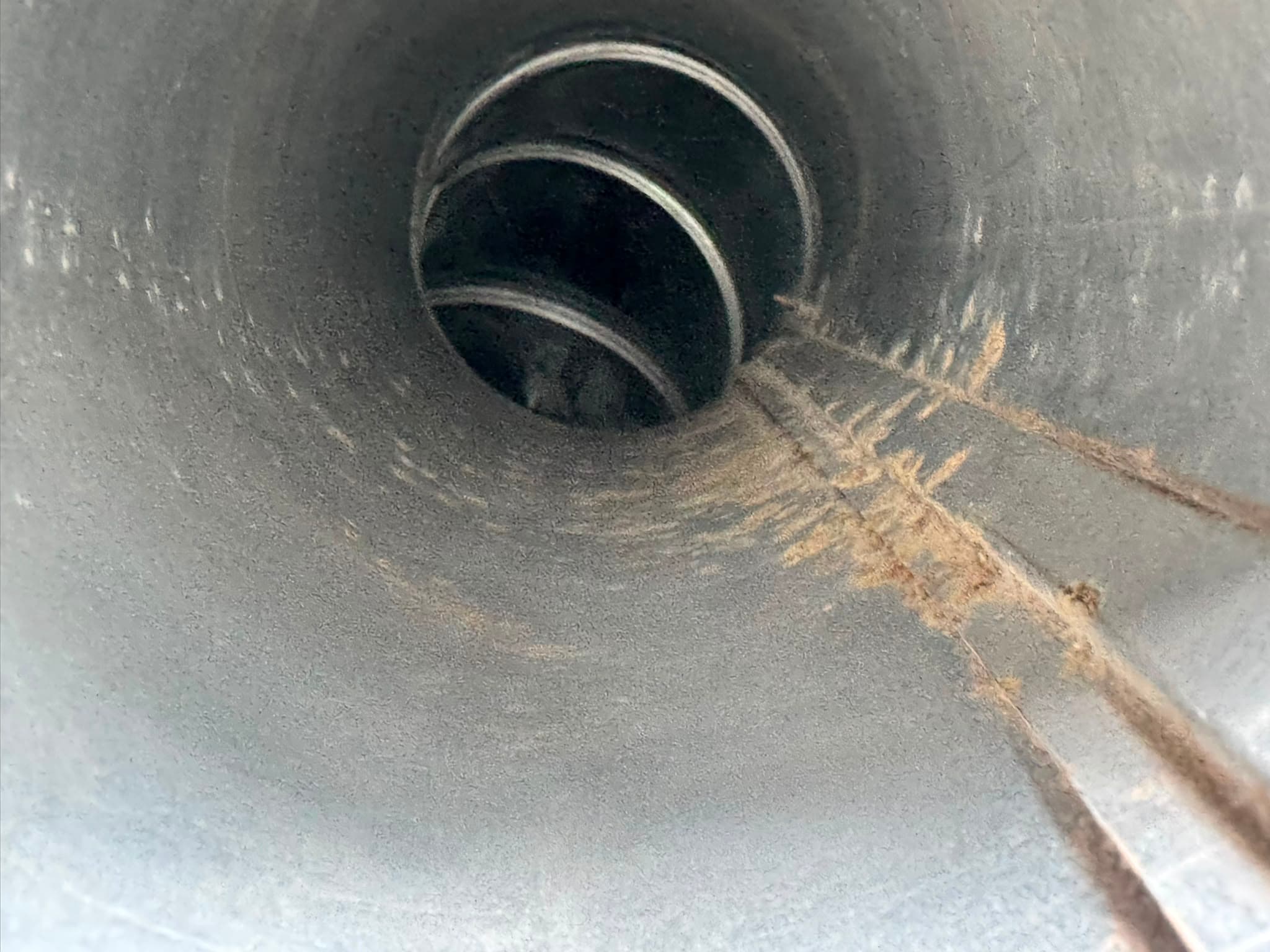 Interior view of a cylindrical metal duct showing a spiral coil and rusted seam.
