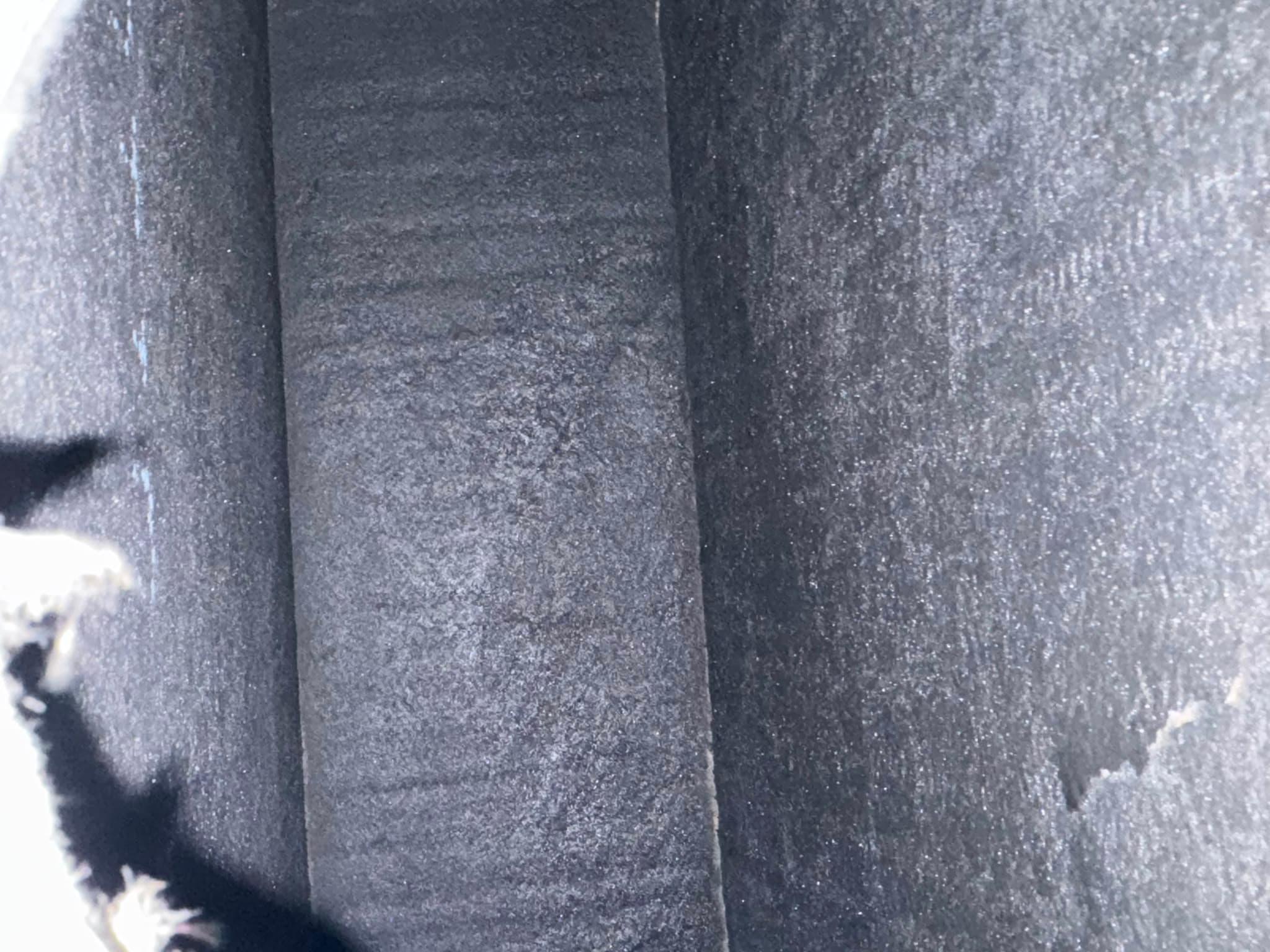 Dark, textured interior of a rectangular chimney flue covered in thick, granular black soot.