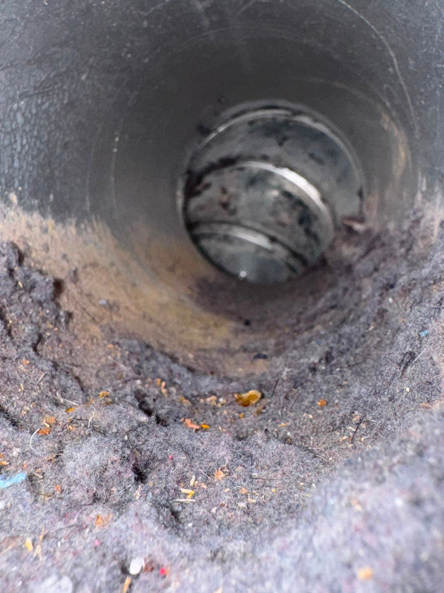 Inside a circular metal dryer vent duct heavily clogged with thick, grey lint and debris.