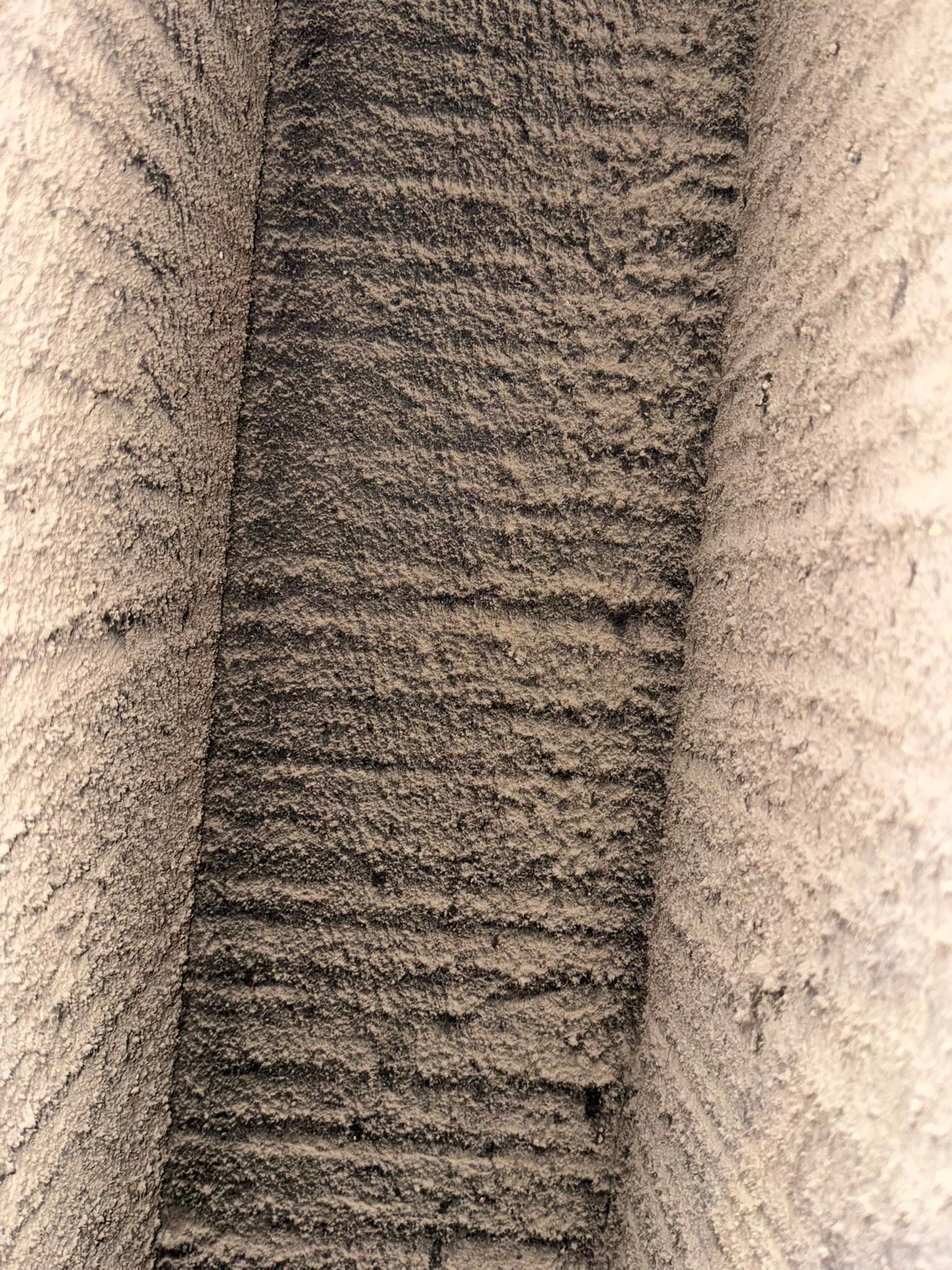 Thick, textured grey dust accumulated in horizontal ridges within a narrow, dark recessed channel.