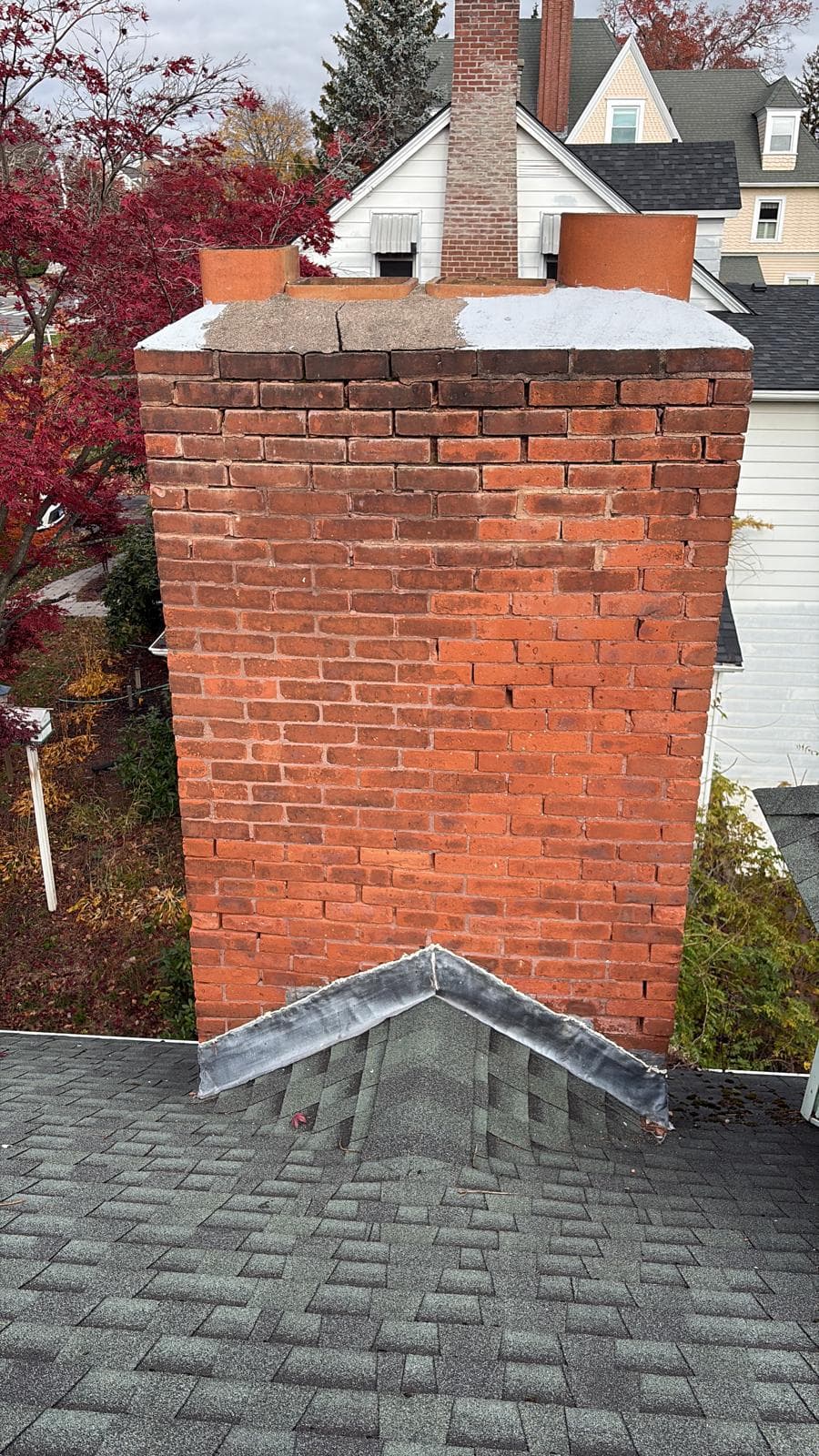 Large red brick chimney with terracotta pots and metal flashing on a grey shingled roof.