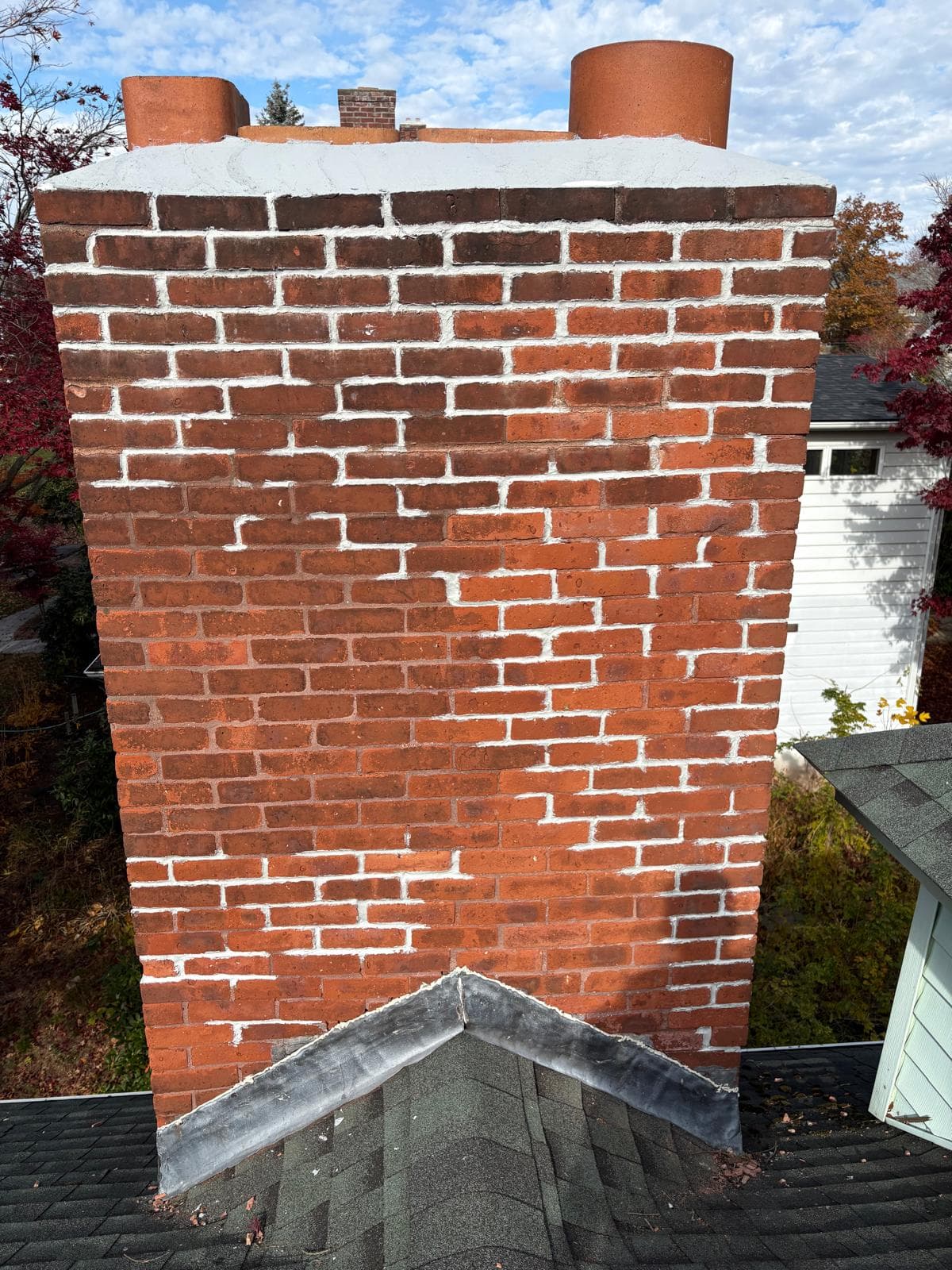 Red brick chimney with white mortar repairs and two clay pots on a shingled roof.