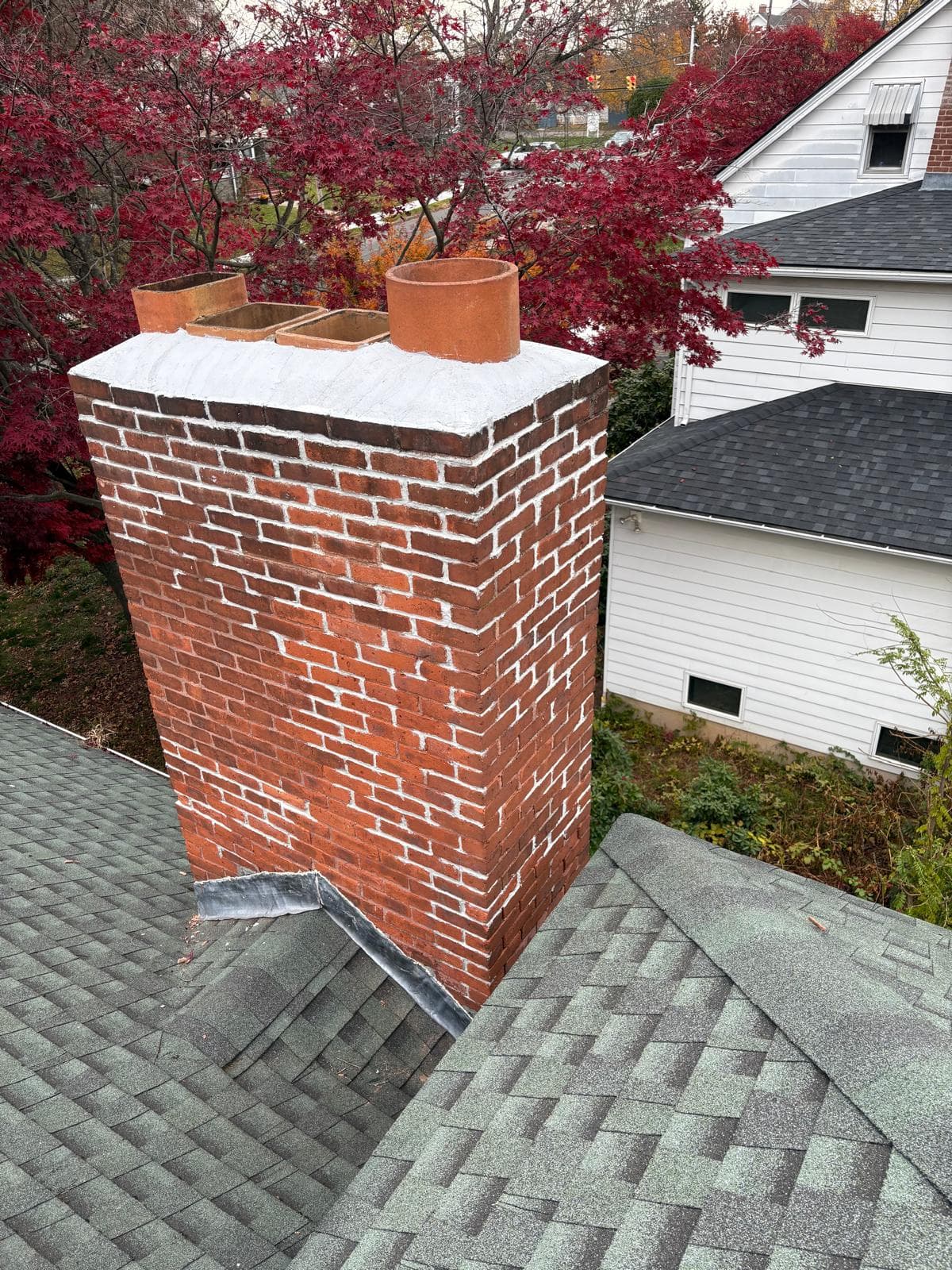 Red brick chimney with white mortar and four clay flues on a grey shingled roof.