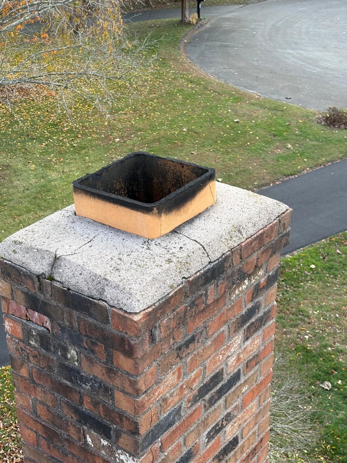 Brick chimney with a cracked concrete crown and a soot-stained square clay flue liner.