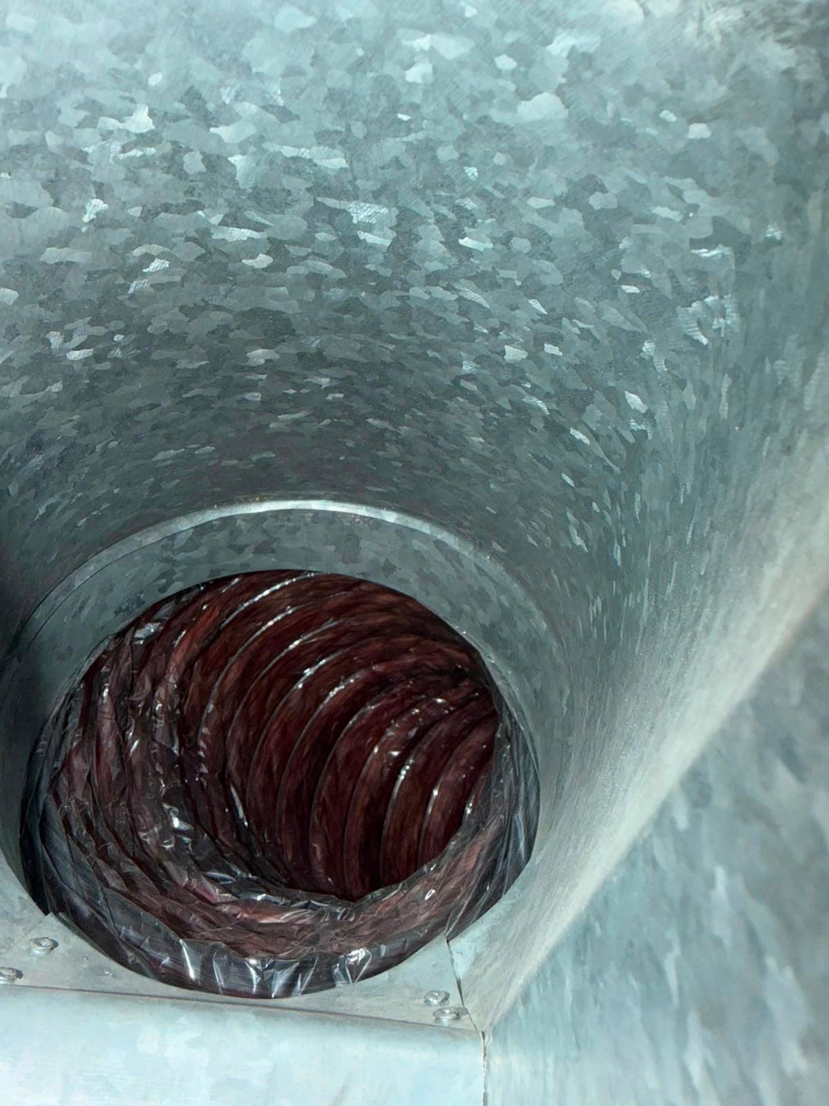 Interior of a galvanized metal duct leading into a dark brown flexible corrugated air hose.