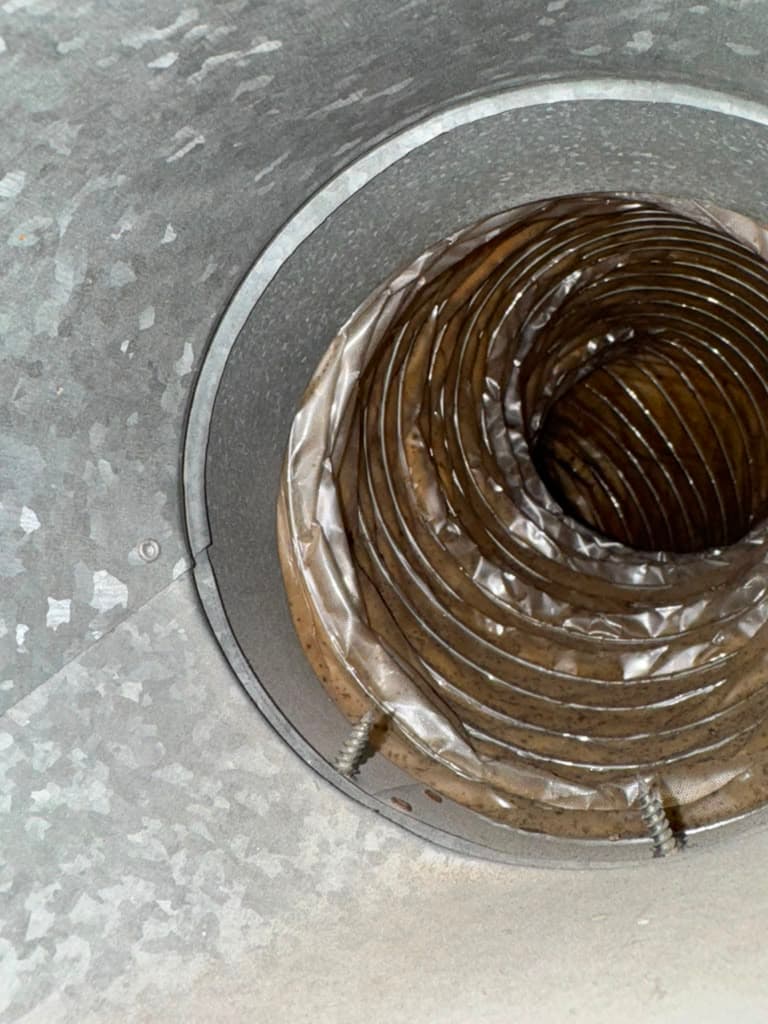 A dirty, flexible brown hose is coiled and secured inside a galvanized metal duct.