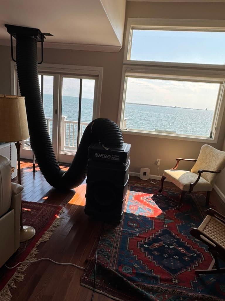 Industrial air scrubber with a large black hose connected to a ceiling vent in a living room.