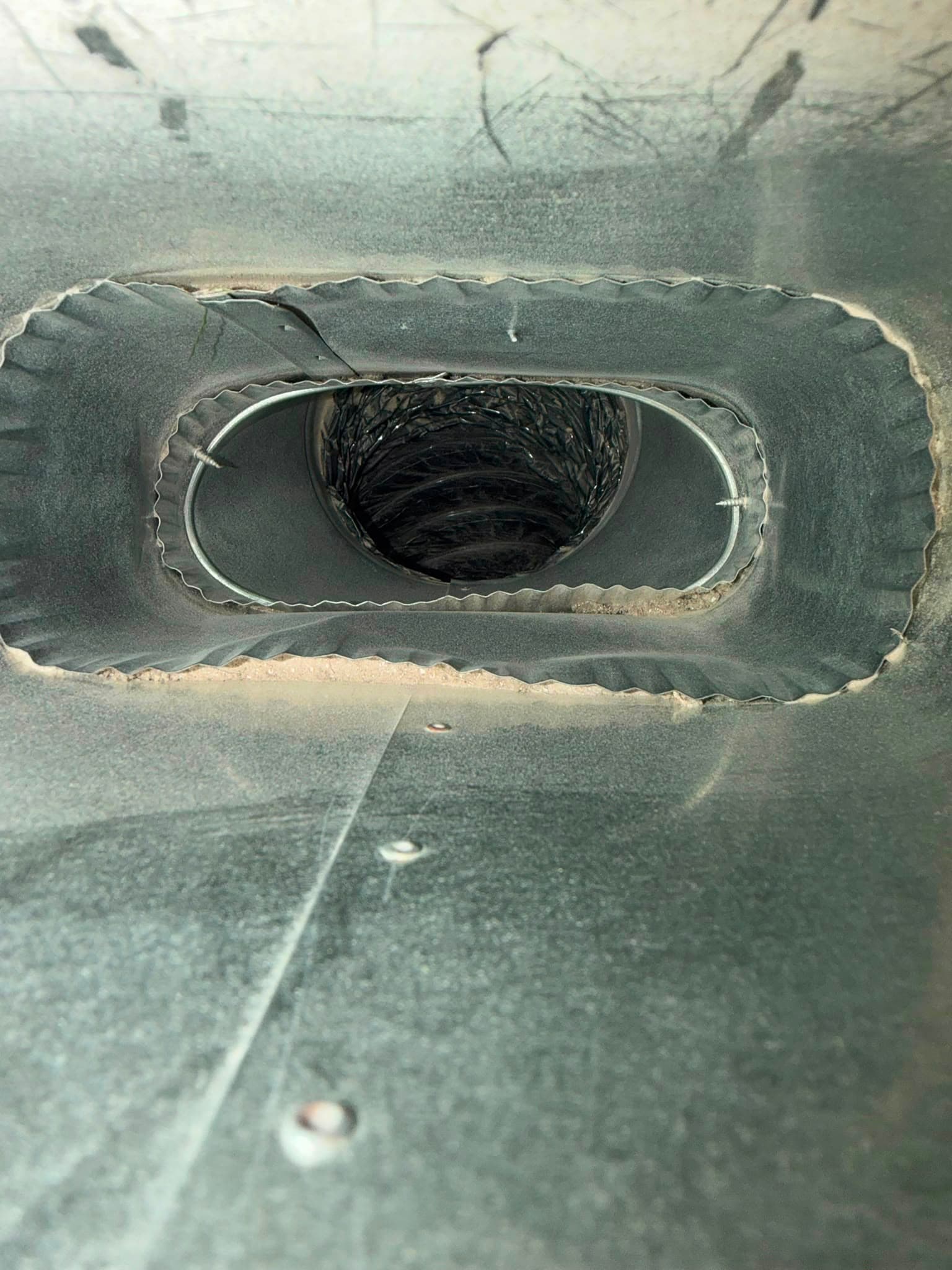 Looking inside a metal air duct at a black flexible vent hose and screws.