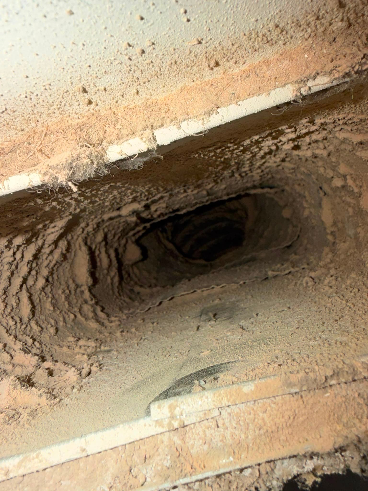 Thick layers of brown dust and debris heavily coating the interior of a rectangular vent.