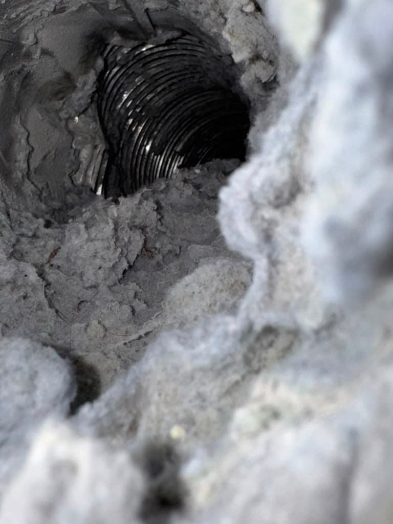 Thick, fuzzy gray lint clogging the interior of a corrugated metal dryer vent duct.