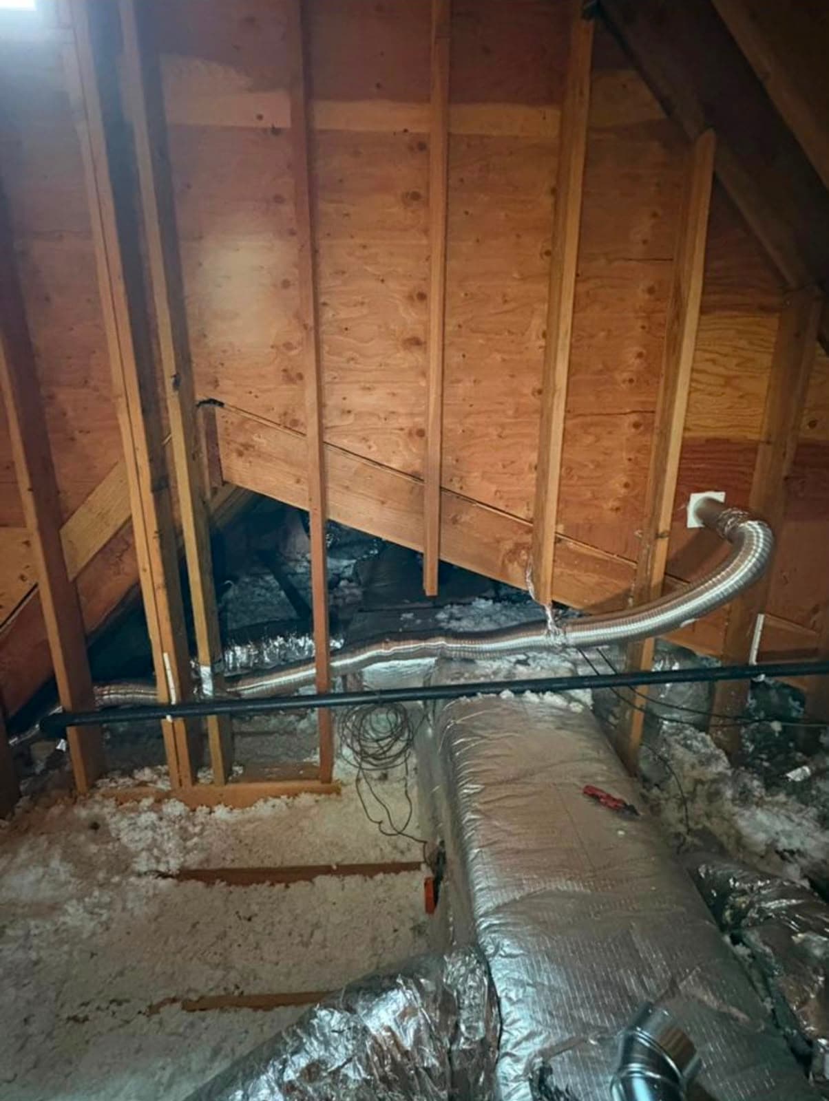 Unfinished attic featuring wooden framing, white insulation, and flexible silver ventilation ducts running across.