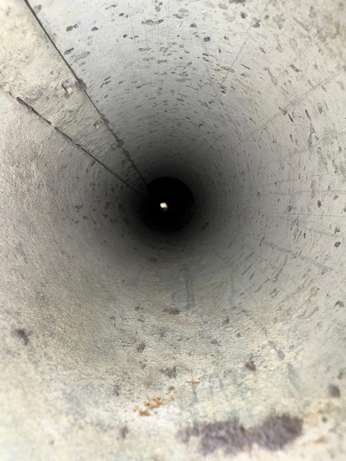 Looking down a long, textured concrete pipe toward a small point of light.