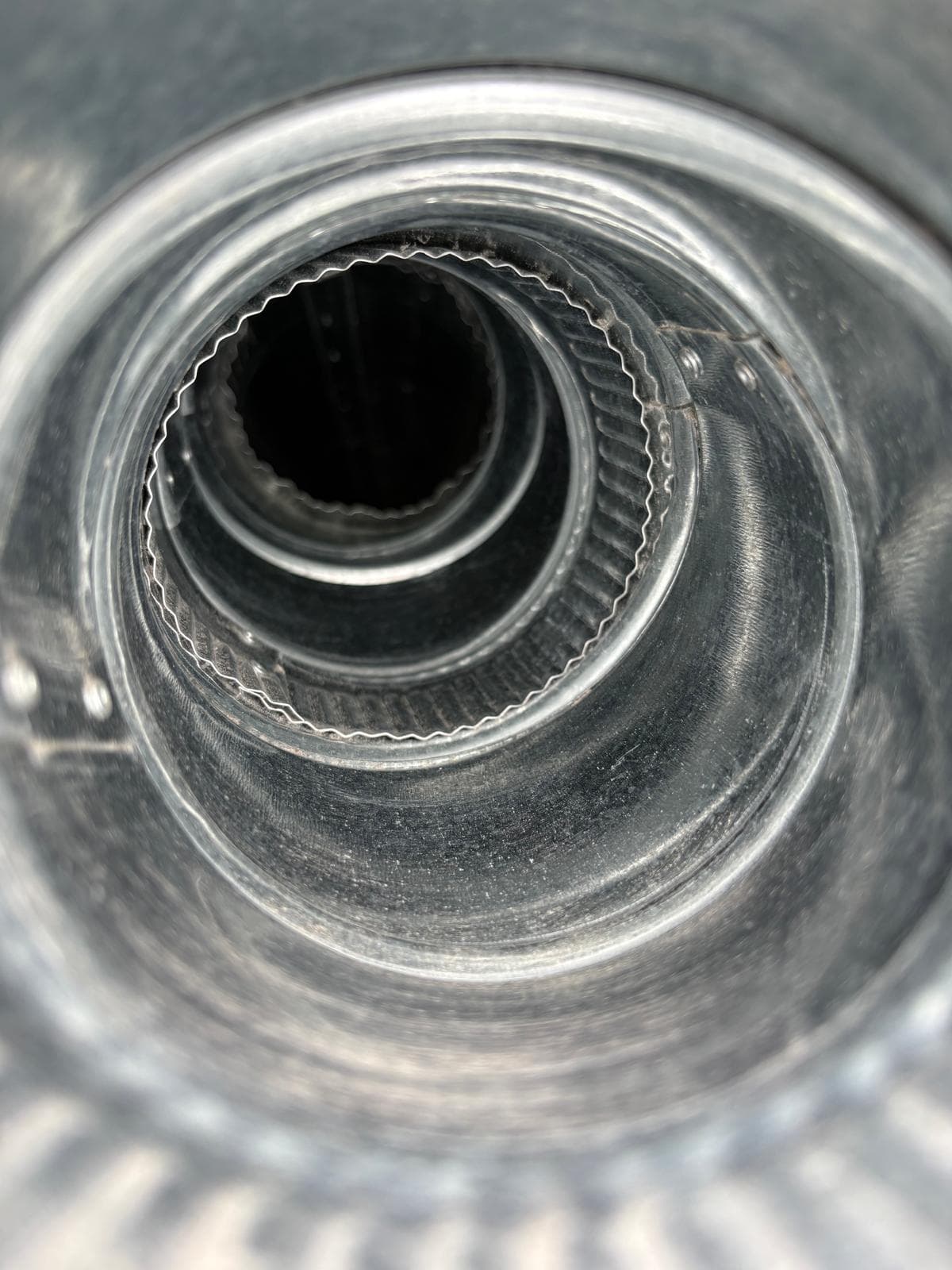 Interior view of nested galvanized metal pipes with crimped edges leading into a dark center.