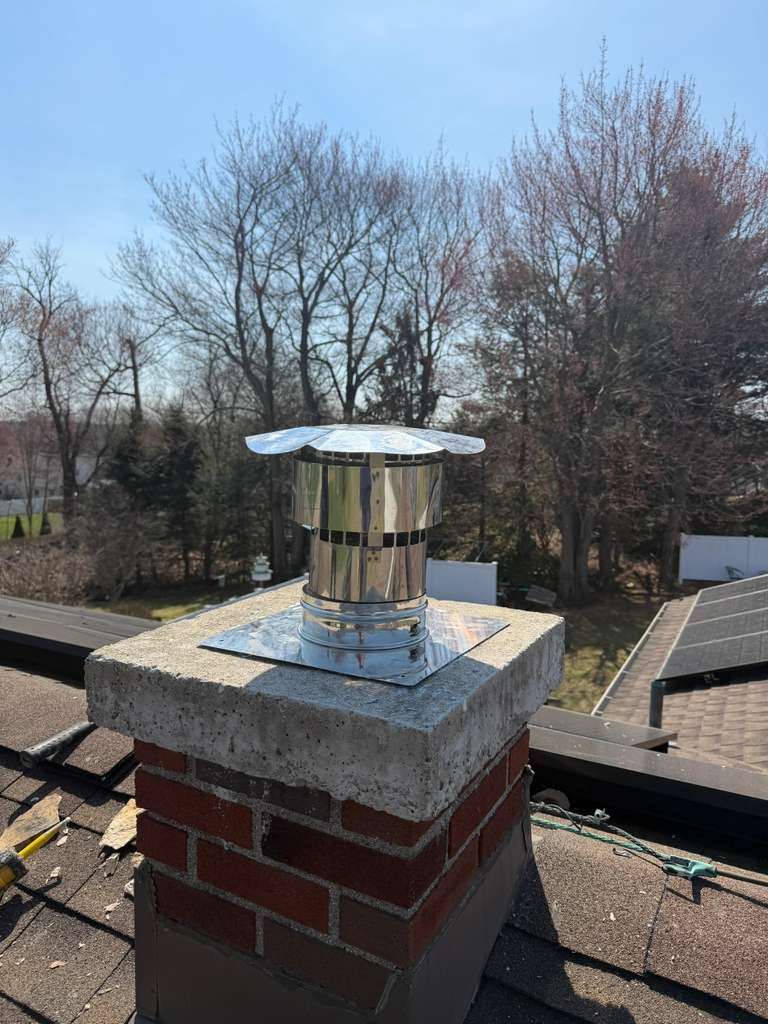 Shiny stainless steel chimney cap mounted on a red brick chimney top outdoors.