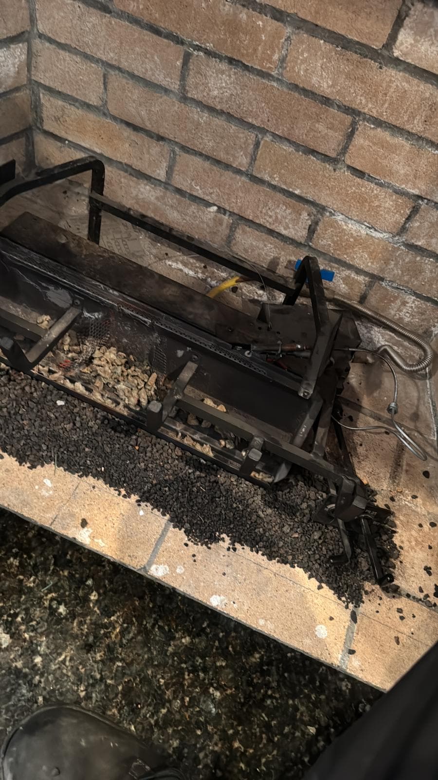Gas fireplace burner assembly with black lava rocks and metal grate inside a brick hearth.