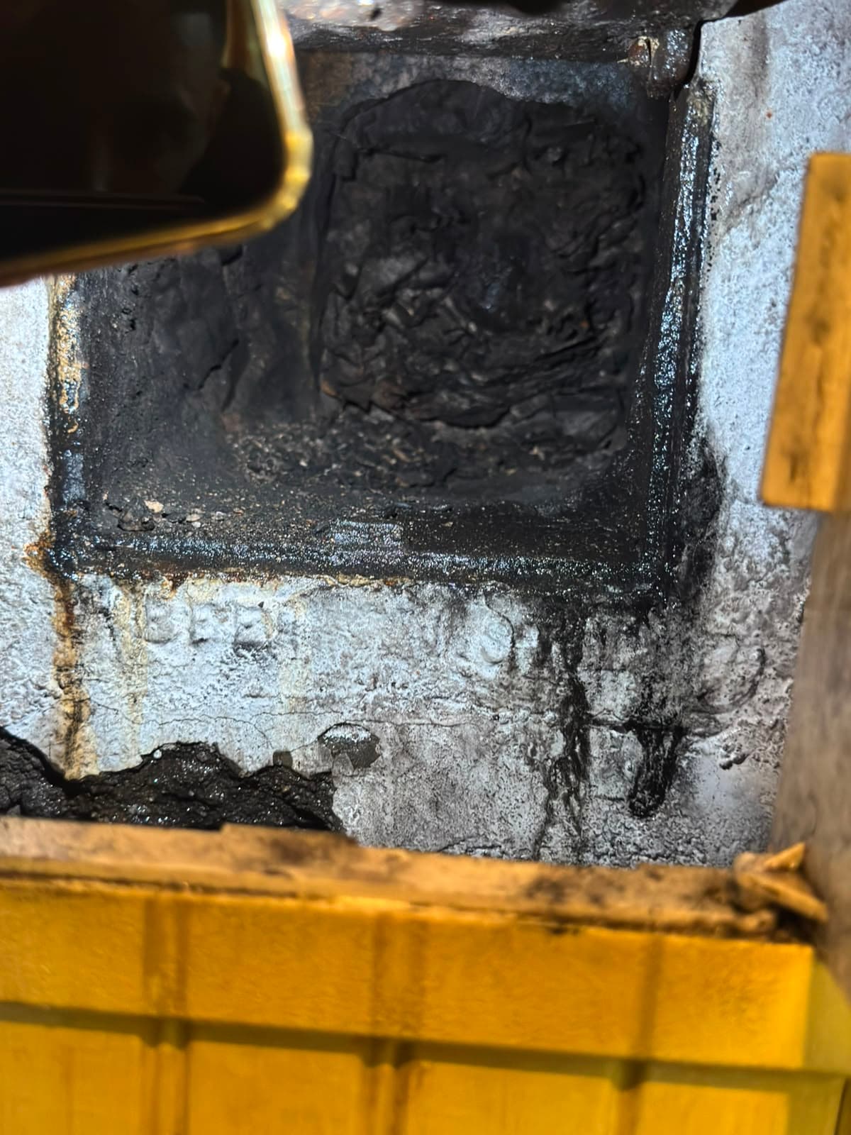 Dark chimney flue heavily clogged with black creosote and soot, surrounded by stained masonry.