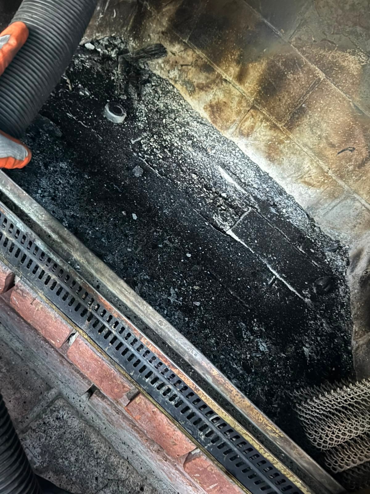 Vacuum hose cleaning thick black soot and ash from the floor of a brick fireplace.