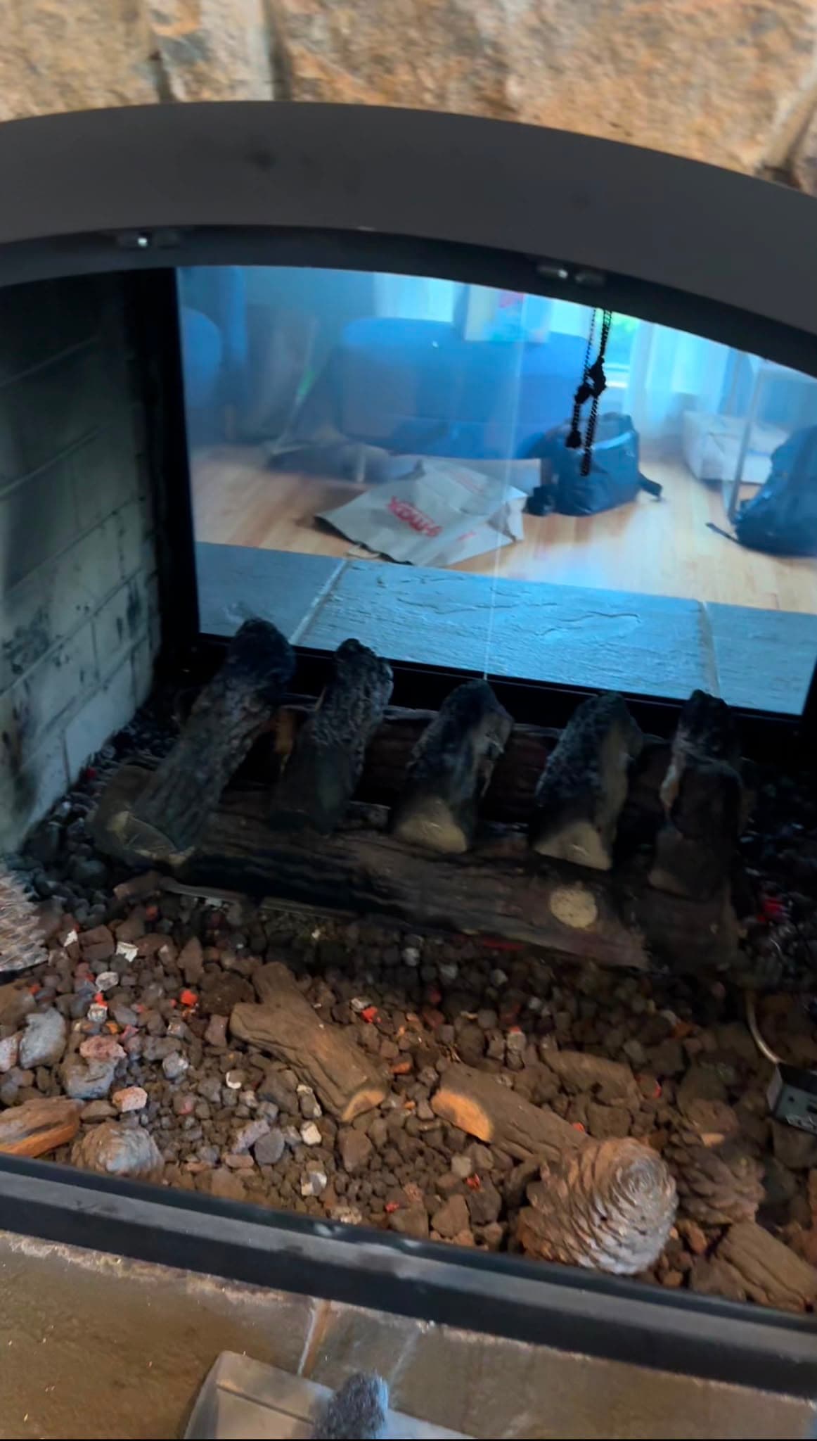 Interior of a gas fireplace with ceramic logs and glowing embers, reflecting a living room.