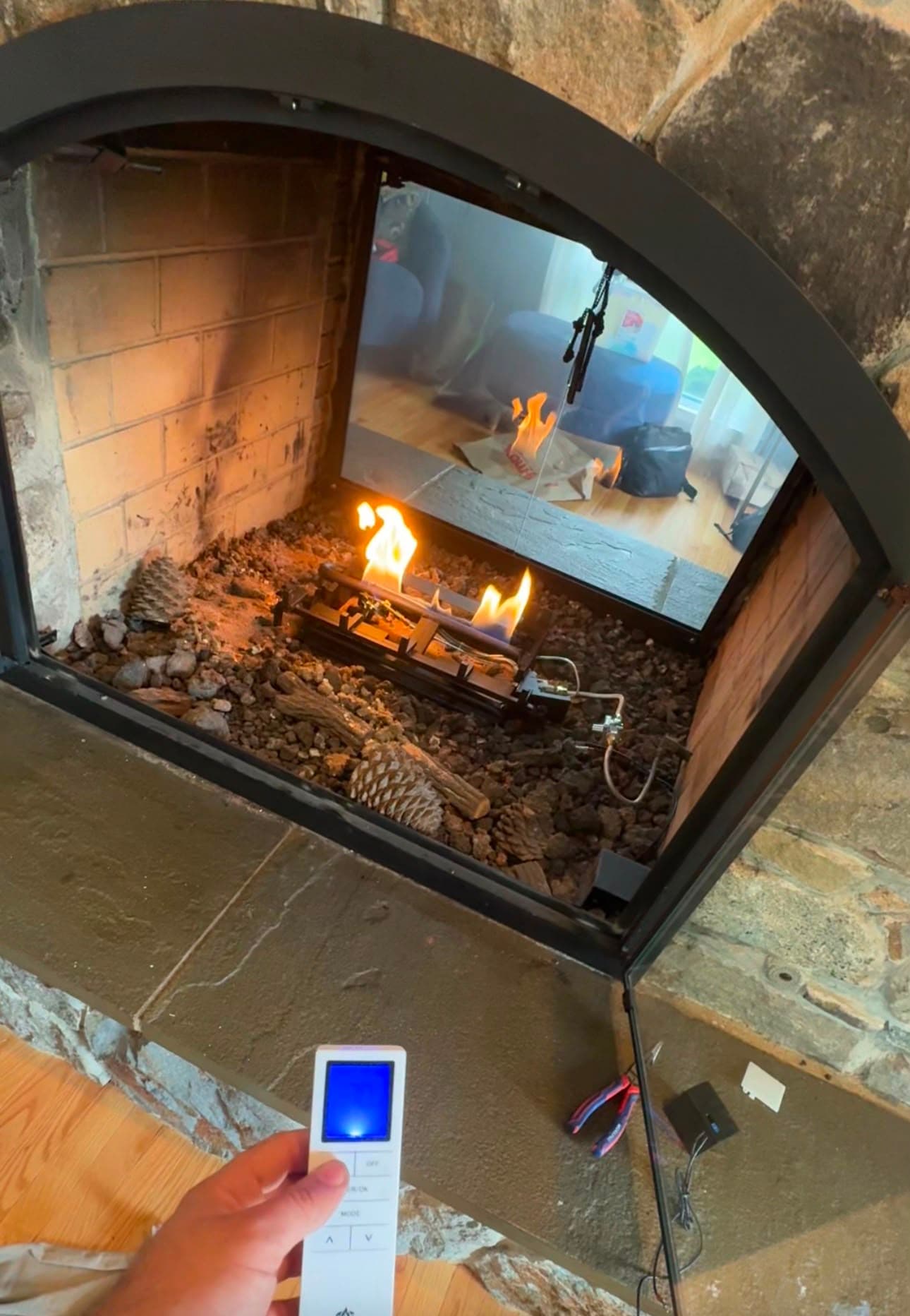 Hand holding a remote control in front of a gas fireplace with small burning flames.